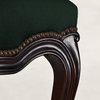 Close-up of a dark green upholstered chair or stool with a carved dark brown wooden frame and a decorative beaded trim along the seat edge.