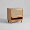 Wooden side table with wicker pattern next to a wooden chair in a room with light-colored tiles.