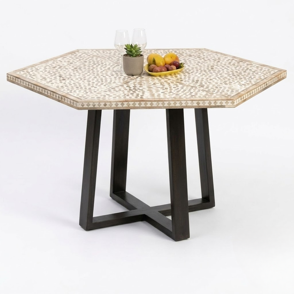 Hexagonal dining table with a beige and white mosaic patterned top and dark brown geometric metal legs, styled with a small plant and fruit on a white background.