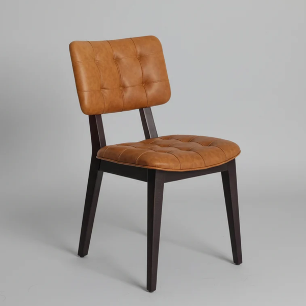 A modern dining chair with a tufted cognac brown leather seat and backrest, supported by a dark brown wooden frame, shown against a neutral gray background.