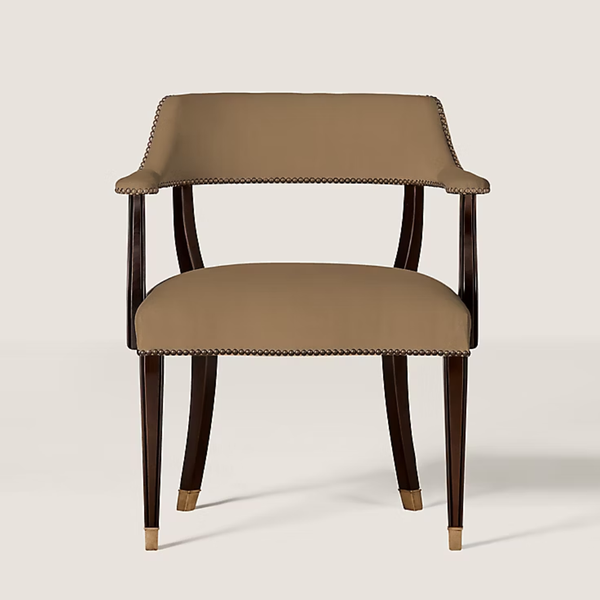 An upholstered armchair with a warm taupe seat and back cushion, dark brown wooden legs, and brass nailhead trim, shown against a light beige background.