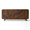A mid-century modern wooden sideboard featuring three doors with large, hand-carved tropical leaf patterns on the front, supported by two short angled legs, shown against a plain white background.