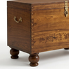 A dark brown wooden chest with turned legs, brass hardware, and floral inlay details on the front, photographed on a light gray studio background.