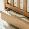 Wooden crib with open drawer revealing a mattress and fitted sheet.