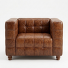 A brown tufted leather armchair with a distressed finish and turned wooden legs, photographed against a plain white background.