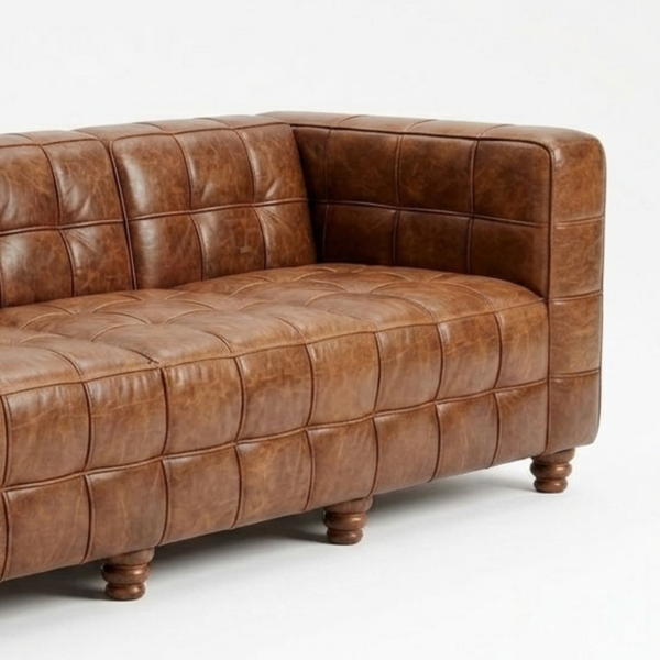 A brown tufted leather sofa with a distressed finish and turned wooden legs, photographed on a clean white background.