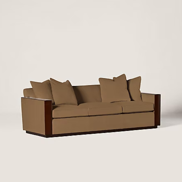 A modern three-seater sofa with tan upholstery and dark brown wooden armrests, shown against a plain light beige background.