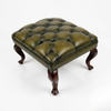 A square tufted leather ottoman stool with an olive green cushion and dark brown carved legs, shown on a white studio background.