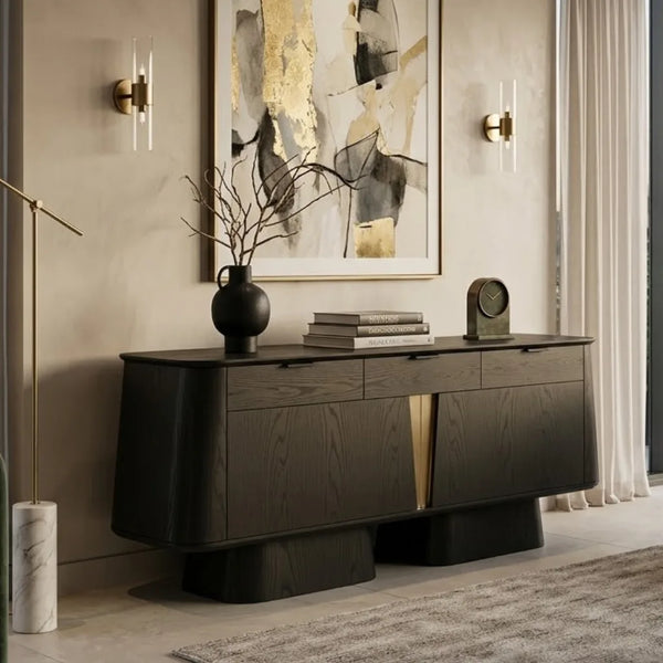 A modern dark wood console table in a styled interior room, decorated with a black vase, books, and a small clock, with wall sconces and abstract wall art behind it.