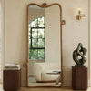 Large floor mirror with wooden frame in a room with a sculpture and books on a side table.