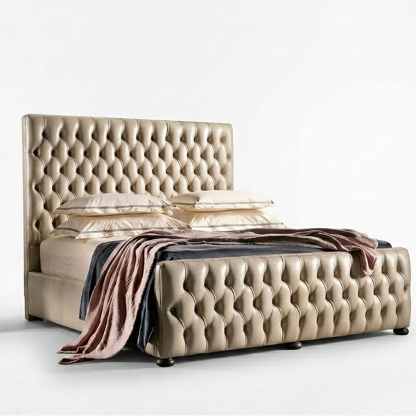 A luxury tufted bed frame in beige leather, styled with matching beige pillows and a draped pink and dark gray throw blanket, set against a plain white studio background.