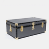 A black vintage-style trunk with gold-tone metal hardware, corner protectors, and rivets, photographed on a light gray background.