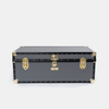A black vintage-style trunk or storage chest with gold-tone metal hardware, corner protectors, and rivets, photographed against a light gray studio background.