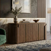 A modern wooden sideboard or credenza in a warm medium brown finish, styled in a contemporary living room setting with a marble backsplash, decorative vase, books, and bowls.
