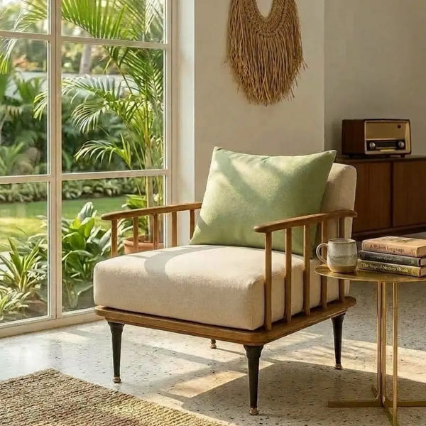 A mid-century modern armchair with cream upholstery and a light green accent pillow, styled in a bright room with a window, side table, and tropical garden view.