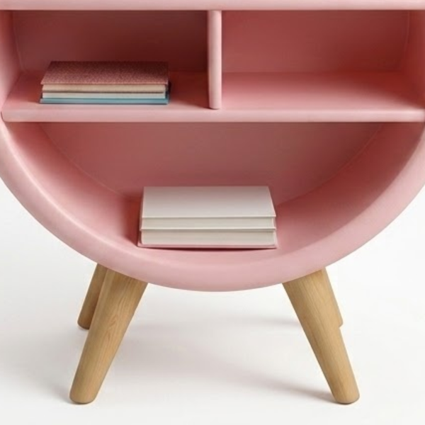 Pink round shelf with wooden legs holding books on a white background