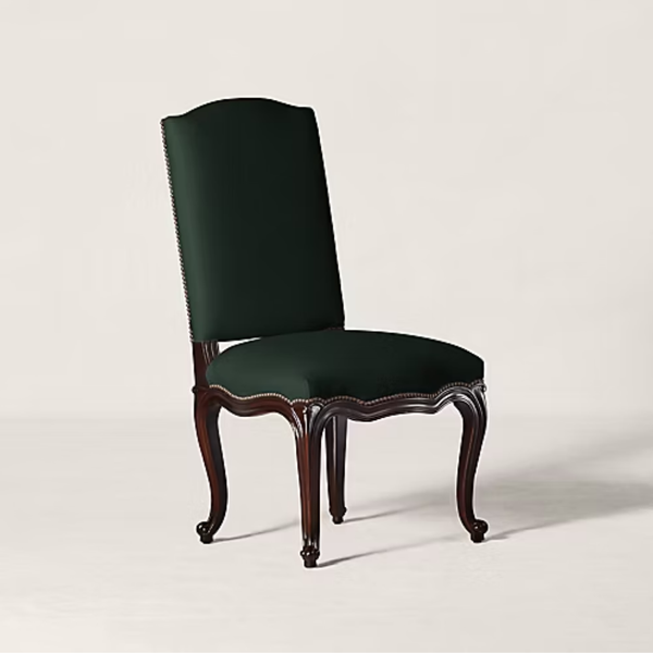 A classic high-back dining chair with dark forest green velvet upholstery and a carved dark brown wooden frame with nailhead trim, shown on a light beige studio background.