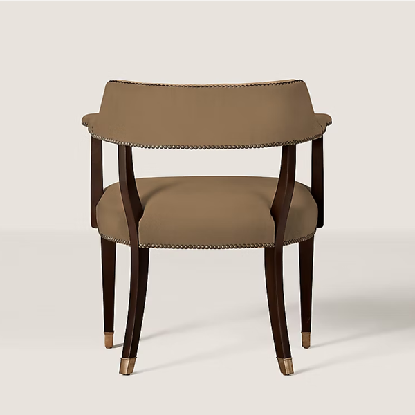 A modern accent chair with a curved taupe upholstered backrest and seat, dark brown wooden legs, and brass nailhead trim and foot caps, shown against a light beige background.