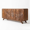A mid-century modern wooden sideboard featuring carved tropical monstera leaf patterns on the front doors, supported by angled legs, shown against a plain white background.