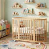 Wooden crib in a child's room with shelves, toys, and a colorful rug.