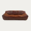 A vintage-style brown leather loveseat sofa with a curved, low-profile silhouette, featuring vertical channel tufting on the backrest and arms, shown against a plain light gray background.