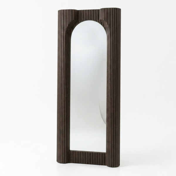 A tall, narrow wall mirror with a dark brown fluted frame, featuring an arched top and bottom, set against a plain white background.