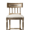 An ornate barstool with a distressed silver-painted frame and a cream upholstered seat cushion, shown against a plain white background.