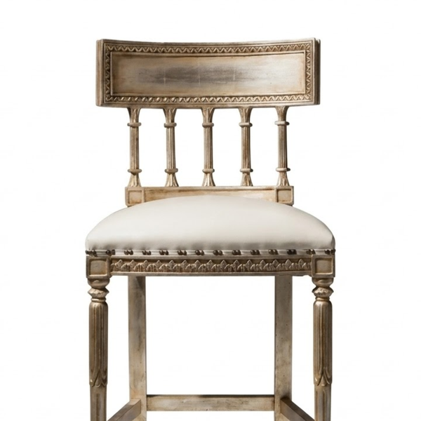 An ornate barstool with a distressed silver-painted frame and a cream upholstered seat cushion, shown against a plain white background.