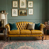 A classic yellow-brown leather Chesterfield sofa with tufted backrest, styled in a living room with dark green walls, framed botanical prints, a patterned rug, and decorative pillows.