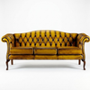 A classic three-seater tufted leather sofa in a rich mustard yellow color, featuring dark brown wooden legs and trim, photographed against a seamless white background.
