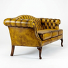 A classic Chesterfield-style leather armchair in a distressed mustard yellow finish, featuring deep button tufting, rolled arms, and dark wooden legs, photographed on a seamless white background.