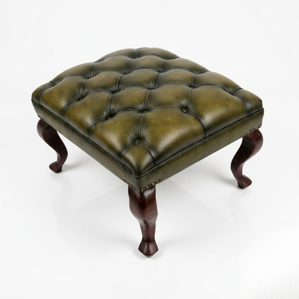 A square tufted leather ottoman stool with an olive green cushion and dark brown carved legs, shown on a white studio background.