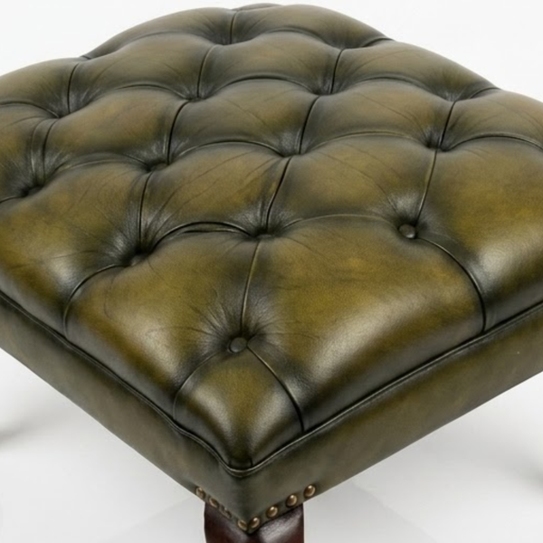 A square tufted leather ottoman in an olive green finish, featuring deep button tufting and a dark wooden leg with brass nailhead trim, shown on a white background.