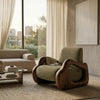 A modern lounge chair with a textured olive green bouclé seat and sculptural dark wood frame, styled in a contemporary living room next to a beige sofa and large windows.