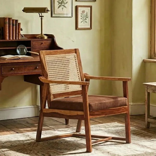 A wooden armchair with a woven cane backrest and a brown upholstered seat cushion, placed in a vintage-style room next to a wooden desk.