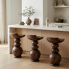 Three wooden stools in front of a marble countertop with decorative items.