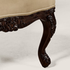 Close-up of an ornate carved wooden chair leg with a dark brown finish and a beige upholstered seat cushion.