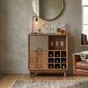 Wooden bar cabinet with wine glasses and bottles in a room with a round mirror and leather chair.
