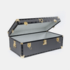 A black hard-shell trunk with gold-tone metal hardware, shown open against a light gray background.