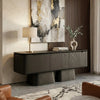 A modern floating media console in a dark wood finish, styled in a contemporary living room setting with a table lamp, books, a ceramic vase, and abstract wall art.