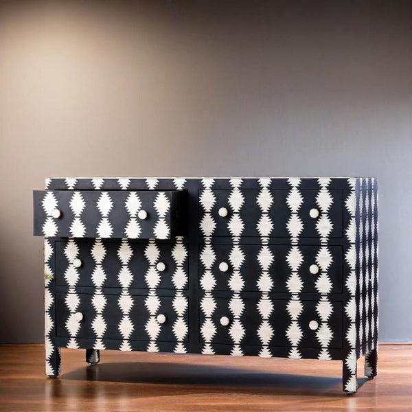 Black dresser with white geometric pattern on a wooden floor against a gray wall