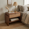 Wooden nightstand with woven drawer next to a bed in a bedroom setting.